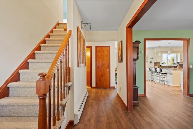 foyer with stairs, a baseboard radiator, wood finished floors, and baseboards