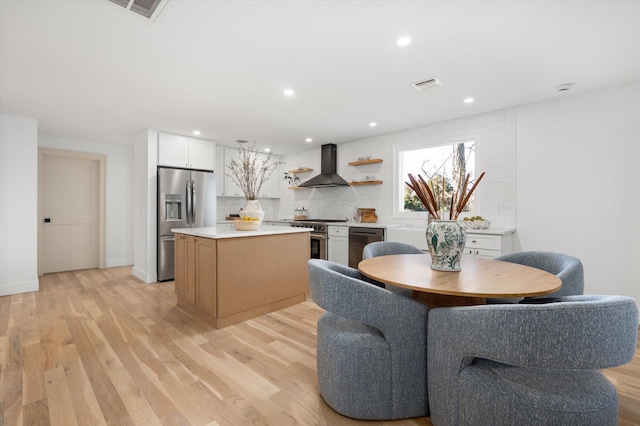 kitchen with light wood finished floors, range hood, visible vents, and stainless steel appliances