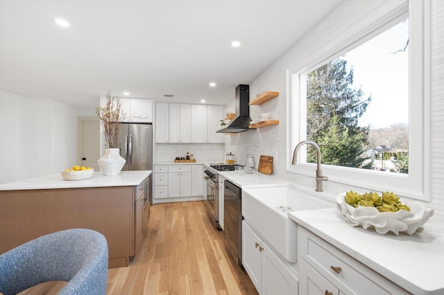 kitchen featuring stainless steel appliances, a sink, white cabinetry, wall chimney range hood, and tasteful backsplash