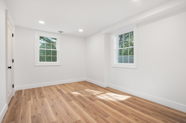 spare room featuring light wood-type flooring, a healthy amount of sunlight, baseboards, and visible vents