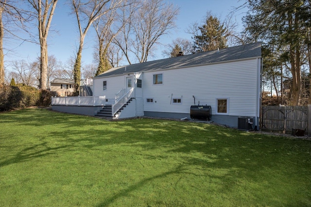 rear view of property with heating fuel, fence, a deck, cooling unit, and a yard