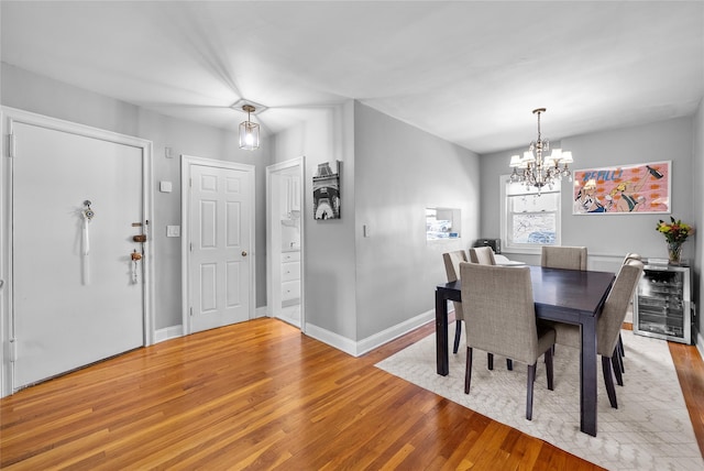 dining area featuring beverage cooler, an inviting chandelier, light wood-style flooring, and baseboards