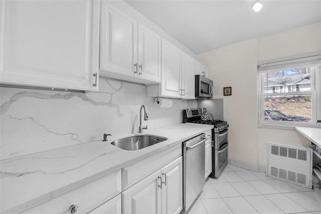 kitchen featuring appliances with stainless steel finishes, radiator, white cabinets, and a sink