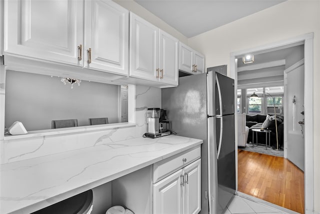 kitchen with white cabinetry, light stone counters, and freestanding refrigerator