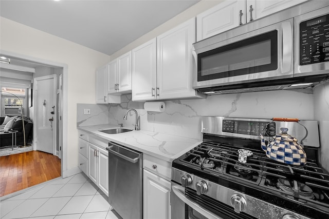 kitchen with light tile patterned floors, a sink, white cabinetry, appliances with stainless steel finishes, and decorative backsplash