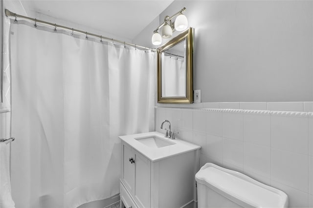 bathroom with tile walls, a shower with shower curtain, toilet, wainscoting, and vanity