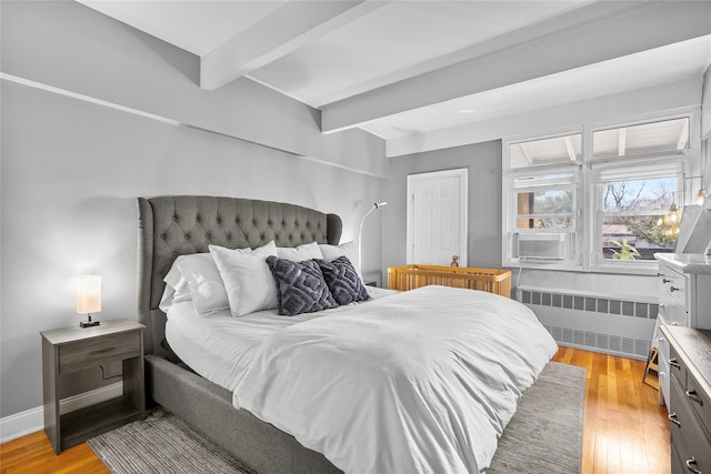 bedroom featuring radiator, light wood-type flooring, baseboards, and beam ceiling