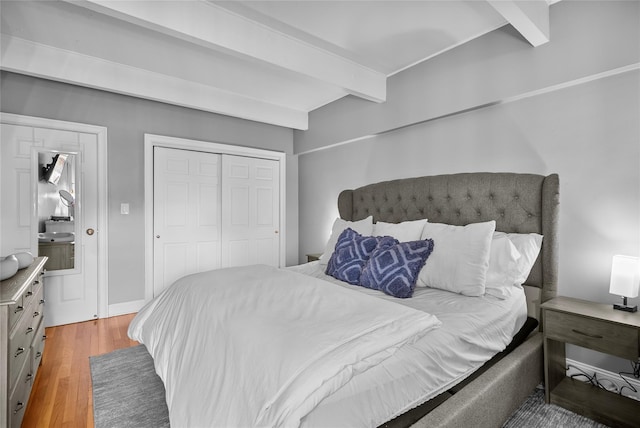 bedroom with a closet, beamed ceiling, wood finished floors, and baseboards