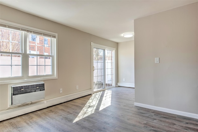 interior space featuring a baseboard heating unit, a wall mounted air conditioner, baseboards, and wood finished floors