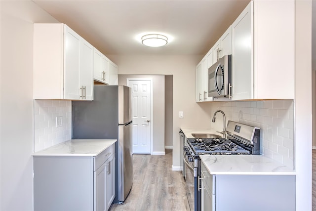 kitchen featuring light wood finished floors, tasteful backsplash, appliances with stainless steel finishes, a sink, and baseboards