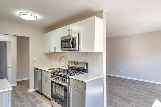 kitchen featuring tasteful backsplash, baseboards, stainless steel appliances, light wood-style floors, and a sink