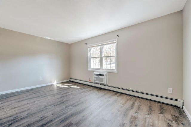 spare room with a baseboard heating unit, a wall unit AC, wood finished floors, and baseboards