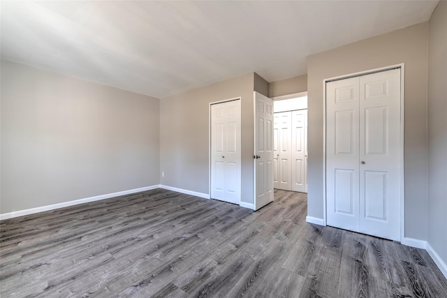 unfurnished bedroom with multiple closets, baseboards, and wood finished floors