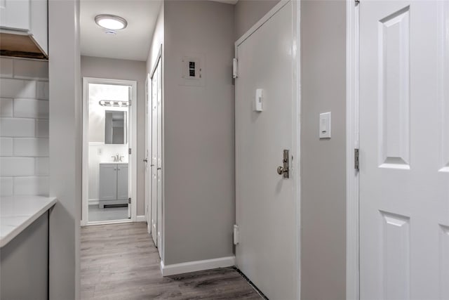 hallway featuring baseboards, a sink, and light wood-style floors