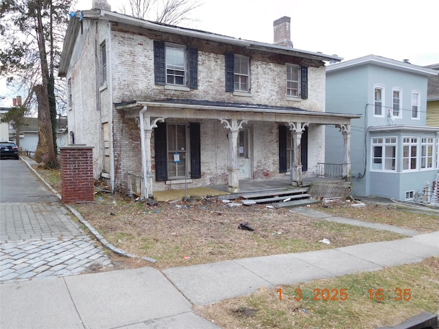 view of front facade featuring covered porch, brick siding, and a chimney