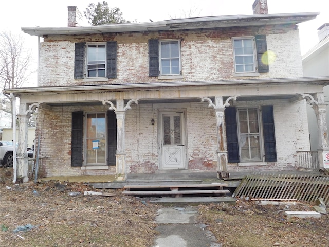 view of front of home featuring a porch, a chimney, and brick siding