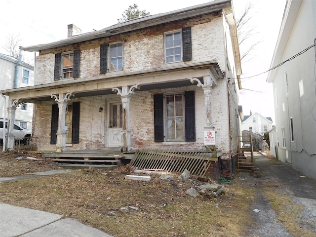 view of front of house featuring a porch, a chimney, and brick siding