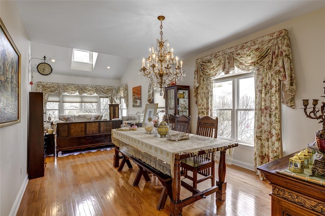 dining room with vaulted ceiling with skylight, light wood-style flooring, and baseboards