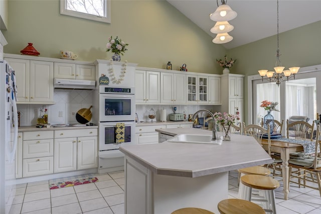 kitchen with white appliances, light tile patterned floors, light countertops, under cabinet range hood, and a sink