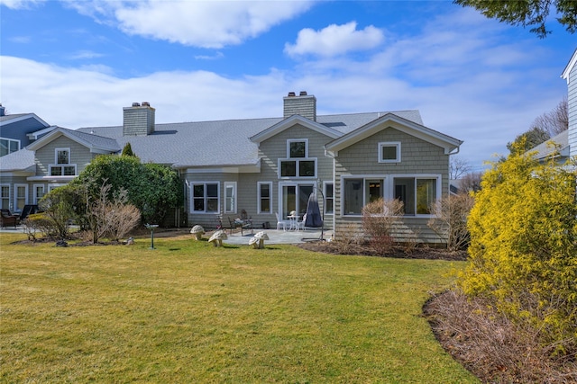 rear view of house featuring a shingled roof, a patio, a chimney, and a lawn