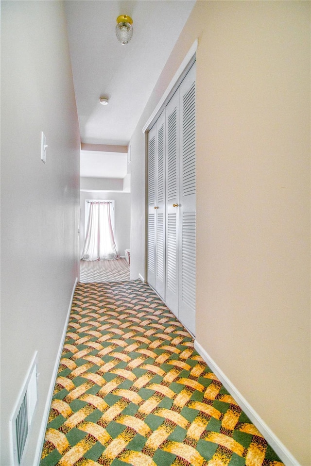 hallway with carpet floors, visible vents, and baseboards