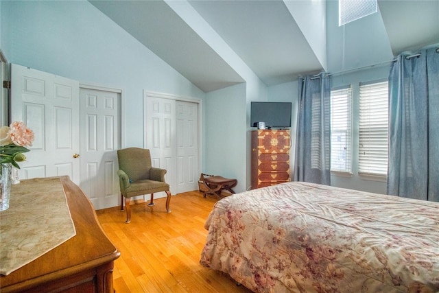 bedroom featuring lofted ceiling, light wood-style flooring, visible vents, and multiple closets