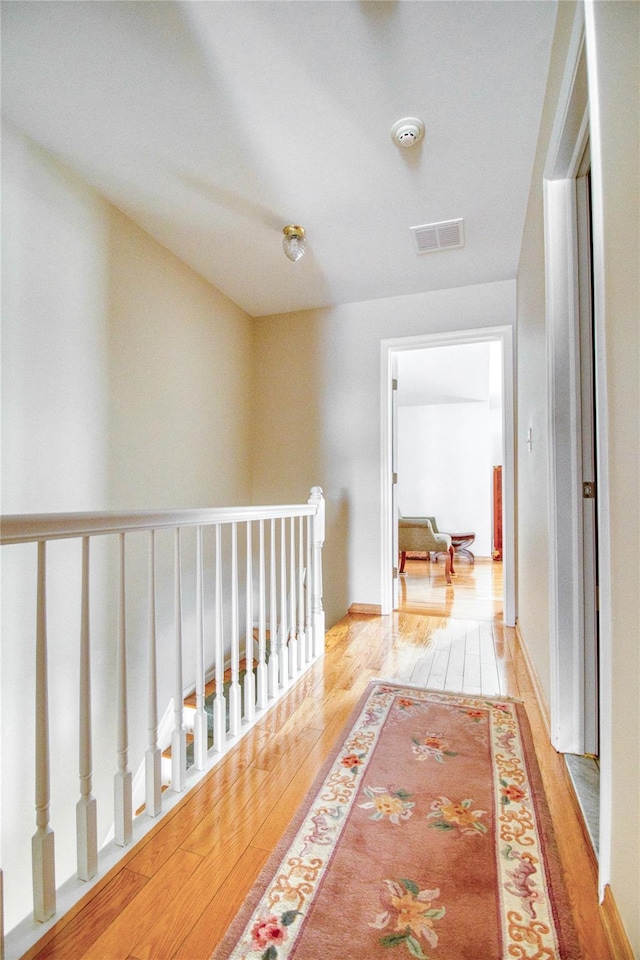 hallway featuring visible vents, an upstairs landing, hardwood / wood-style flooring, and baseboards