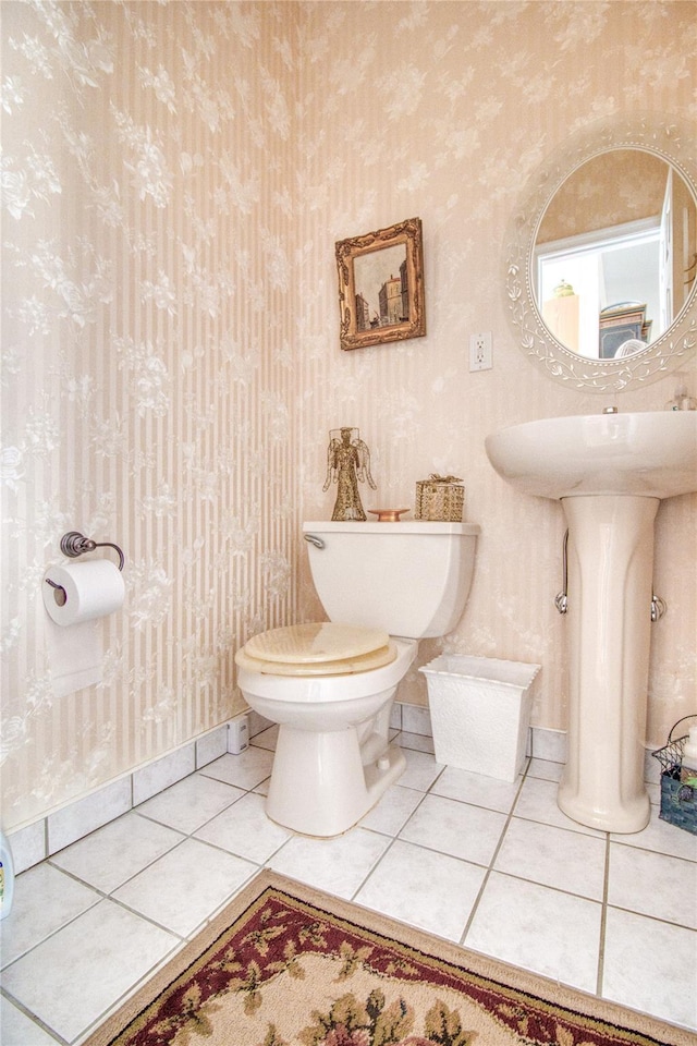 half bathroom with baseboards, wallpapered walls, toilet, and tile patterned floors