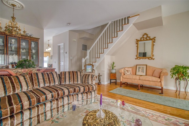 living area featuring visible vents, baseboards, stairway, wood finished floors, and an inviting chandelier