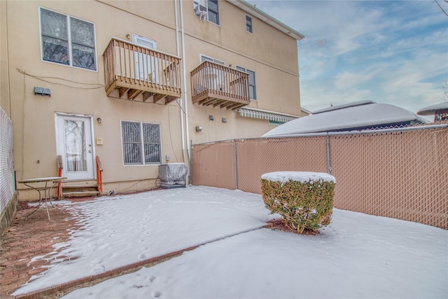 snow covered patio with entry steps, fence, and a balcony