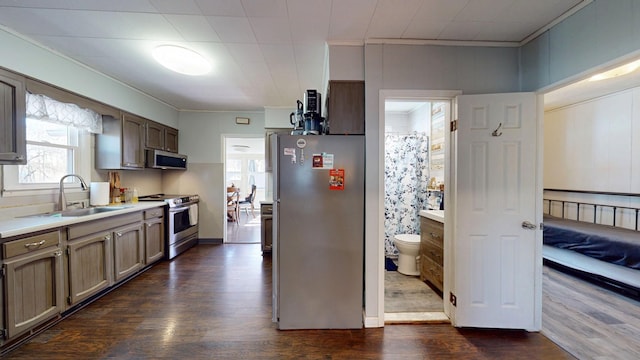 kitchen featuring dark wood finished floors, stainless steel appliances, crown molding, light countertops, and a sink