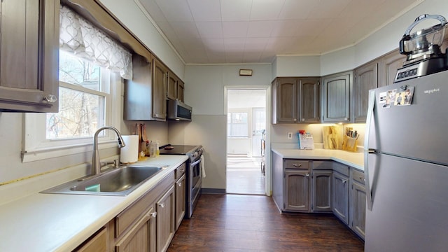 kitchen with dark wood-style floors, light countertops, appliances with stainless steel finishes, ornamental molding, and a sink