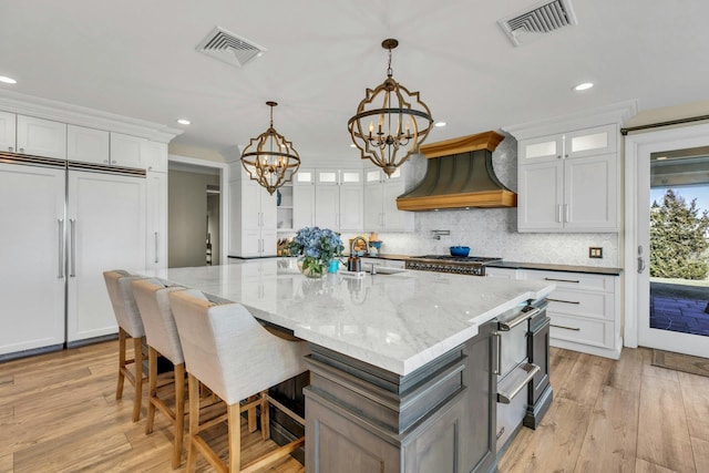 kitchen featuring visible vents, paneled refrigerator, a notable chandelier, and custom exhaust hood