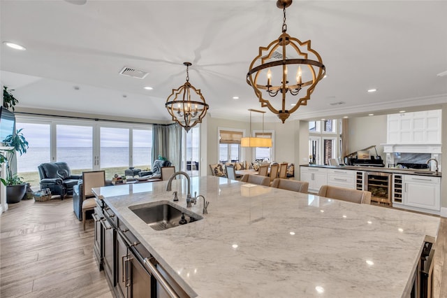 kitchen featuring visible vents, white cabinets, open floor plan, a sink, and a notable chandelier