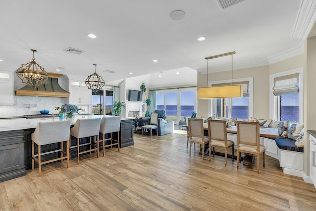 kitchen with light wood-style flooring, premium range hood, white cabinets, tasteful backsplash, and a kitchen bar