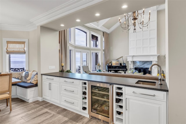 bar featuring beverage cooler, ornamental molding, a sink, light wood-type flooring, and a notable chandelier