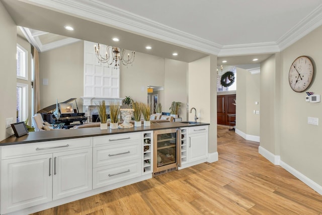 bar with baseboards, wine cooler, ornamental molding, light wood-type flooring, and a sink