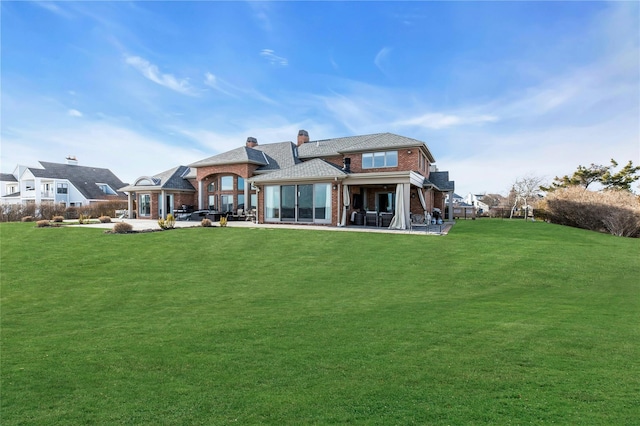 back of house with brick siding, a patio, a chimney, and a lawn