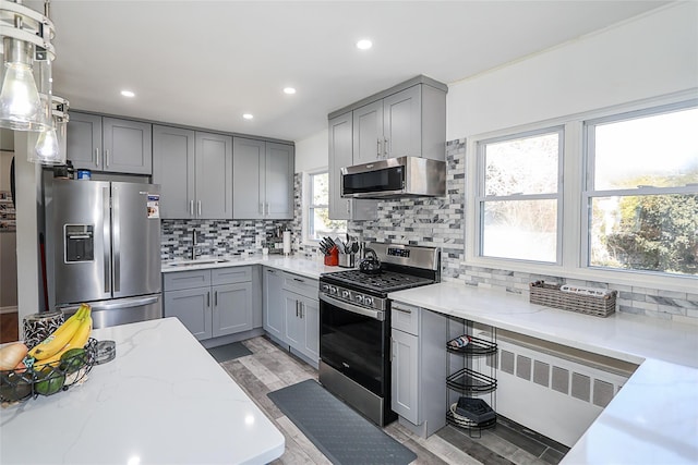 kitchen with stainless steel appliances, gray cabinets, a sink, and light stone countertops