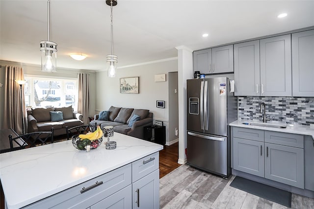 kitchen with open floor plan, a sink, gray cabinets, stainless steel refrigerator with ice dispenser, and backsplash