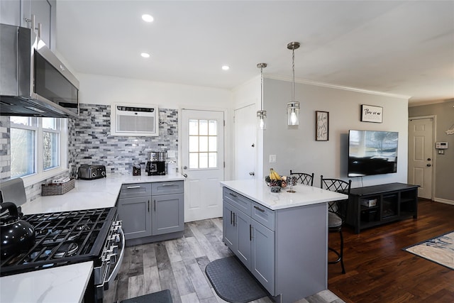 kitchen with range with gas stovetop, stainless steel microwave, gray cabinetry, a wall mounted air conditioner, and a kitchen breakfast bar