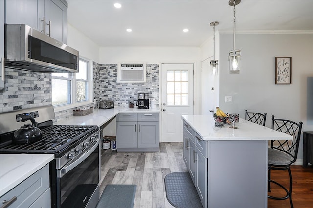 kitchen with stainless steel appliances, tasteful backsplash, gray cabinetry, light wood-style floors, and a kitchen bar