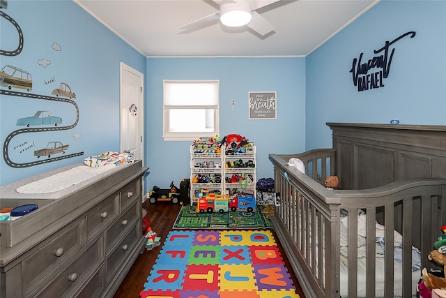 bedroom with a crib, crown molding, ceiling fan, and dark wood-type flooring