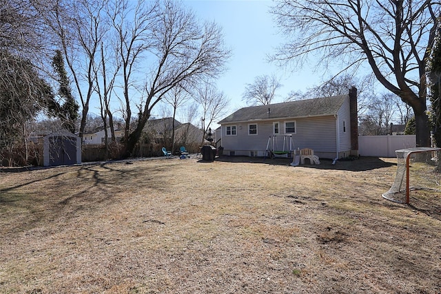 rear view of house featuring a shed, a chimney, fence, and an outbuilding