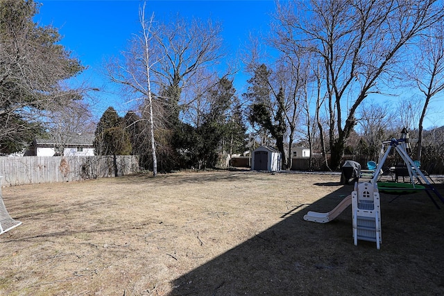 view of yard featuring playground community, an outdoor structure, fence, and a storage unit