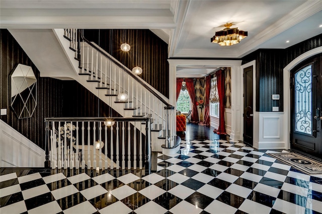 foyer featuring stairs, ornamental molding, a chandelier, a wainscoted wall, and a decorative wall