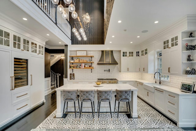 kitchen featuring wall chimney range hood, white cabinets, a sink, and open shelves