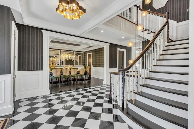 foyer featuring stairs, ornamental molding, wallpapered walls, a notable chandelier, and wainscoting