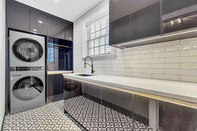 clothes washing area featuring stacked washer and clothes dryer, cabinet space, and a sink