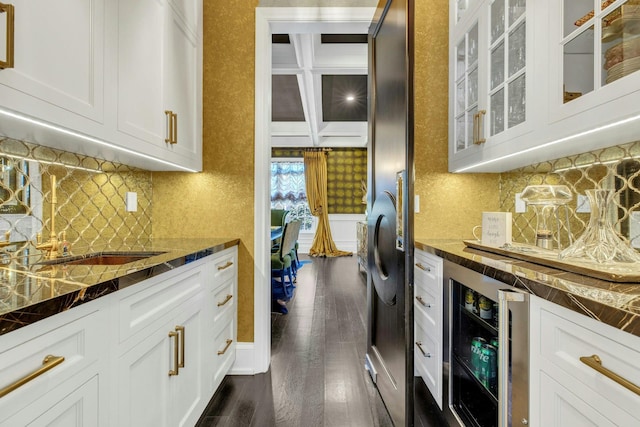 kitchen with dark wood-type flooring, beamed ceiling, beverage cooler, white cabinets, and glass insert cabinets